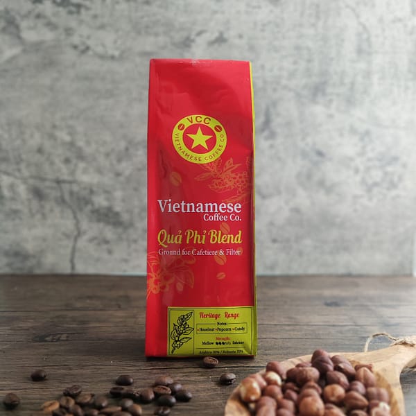 A bag of Qua Phi blend Vietnamese coffee. Pictured with a scoop of hazelnuts and some Vietnamese Coffee beans spilled on a table.