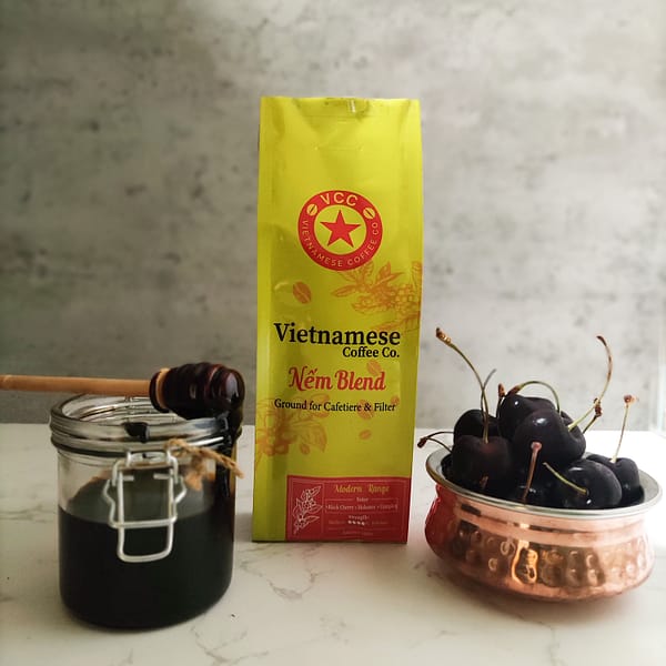 A bag of Nem blend Vietnamese coffee. Pictured with a jar of molasses and a copper bowl of black cherries.
