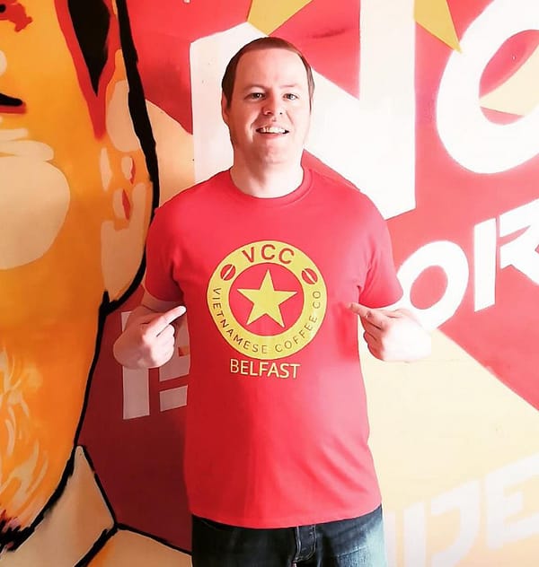 A man wearing a Vietnamese Coffee Co. branded t-shirt. The t-shirt is red and has a yellow circular Vietnamese Coffee Co. logo.