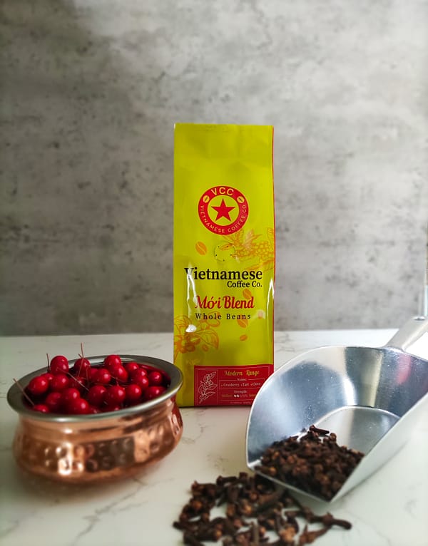 A bag of Moi blend Vietnamese coffee. Pictured with a copper bowl of cranberries and a metal scoop of cloves.